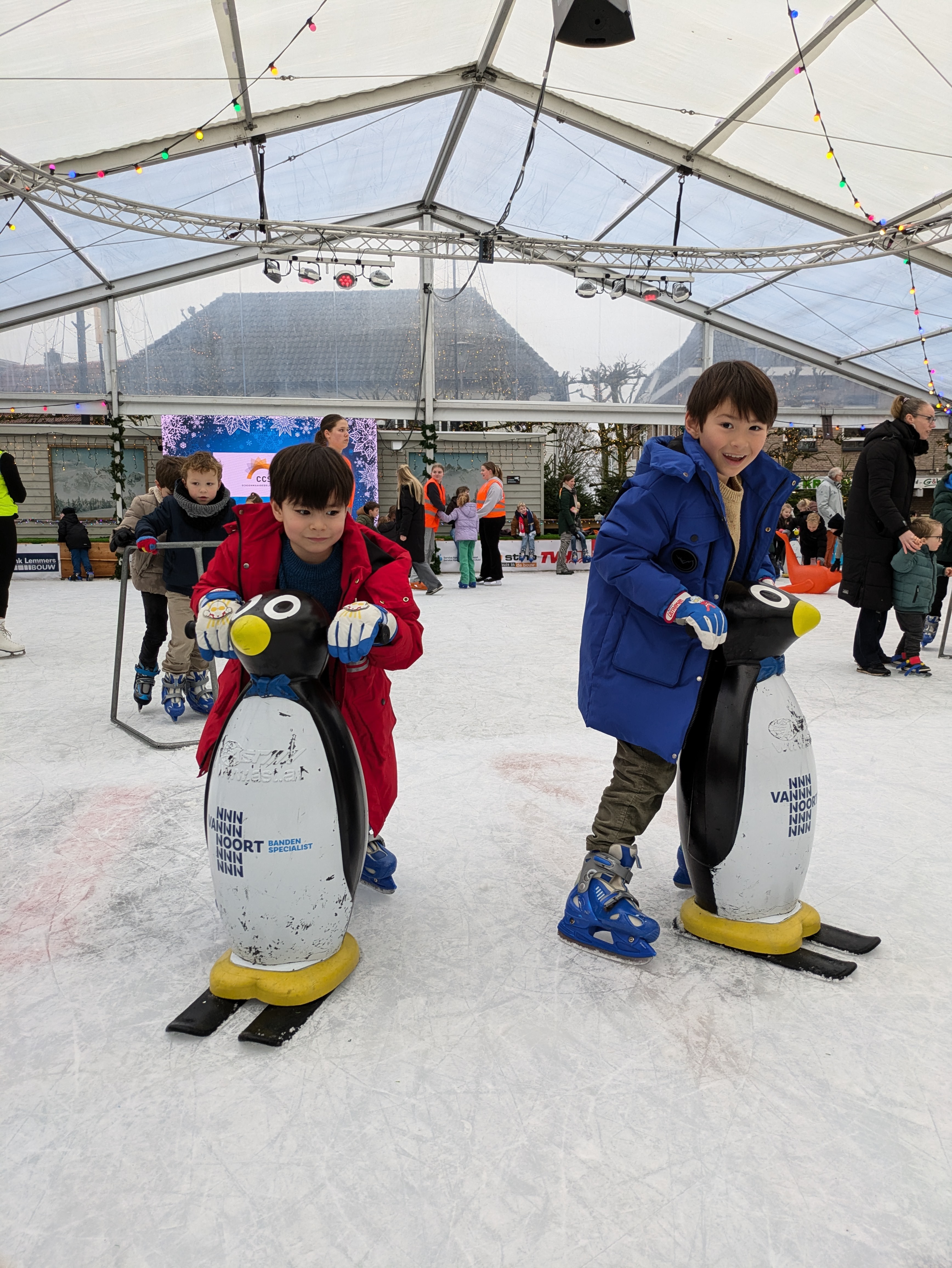 Two boys learning to ice skate with penguin skating aids at a winter event